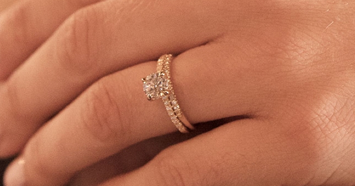 Woman's hand wearing a round diamond engagement ring and round diamond wedding band.